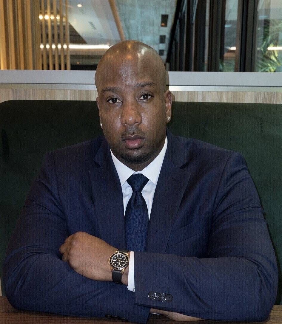 Jevaughn Laing in a navy suit, arms folded, seated at a table
