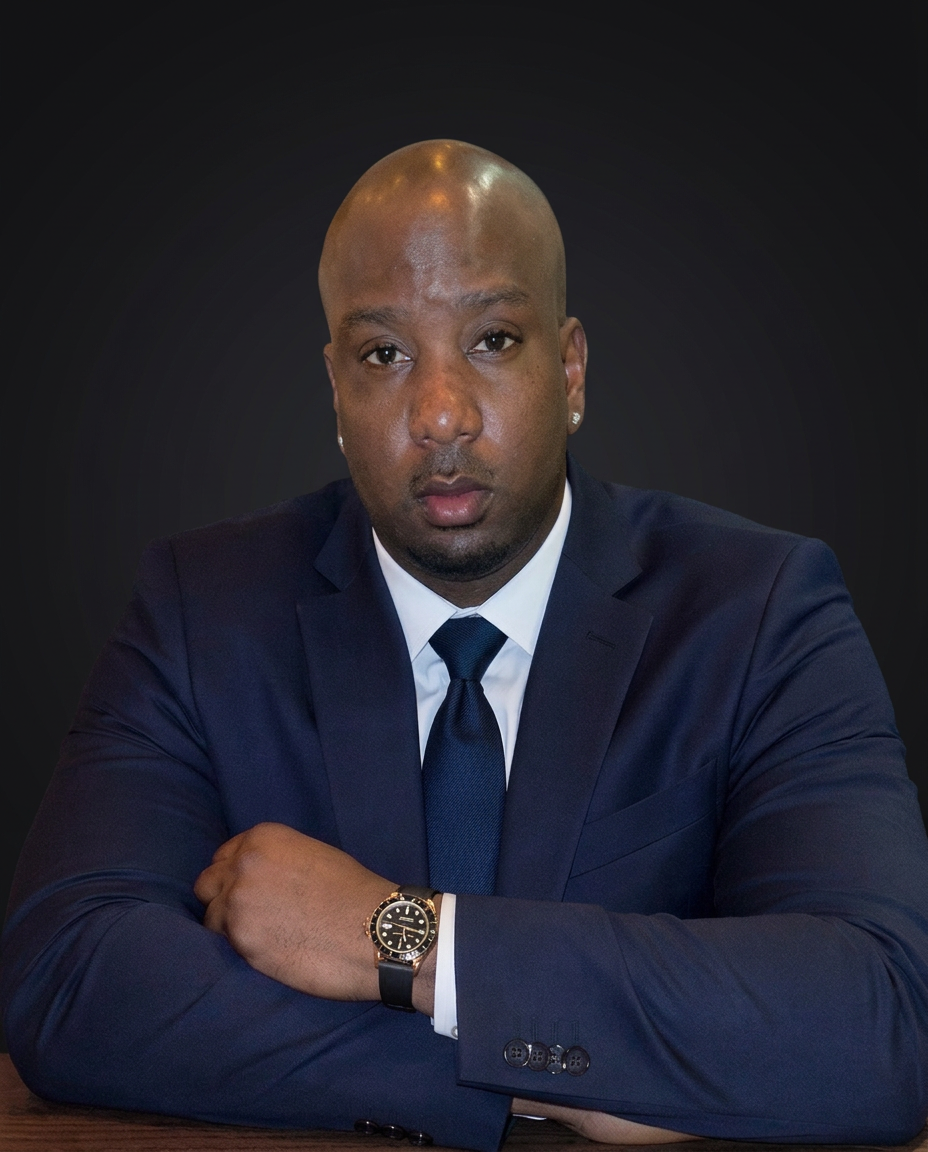 Jevaughn Laing in a navy suit, arms folded, seated at a table